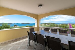 A dining area with a table and chairs, overlooking a scenic view of the sea and hills. - Modern Villa with Pool (Blato)