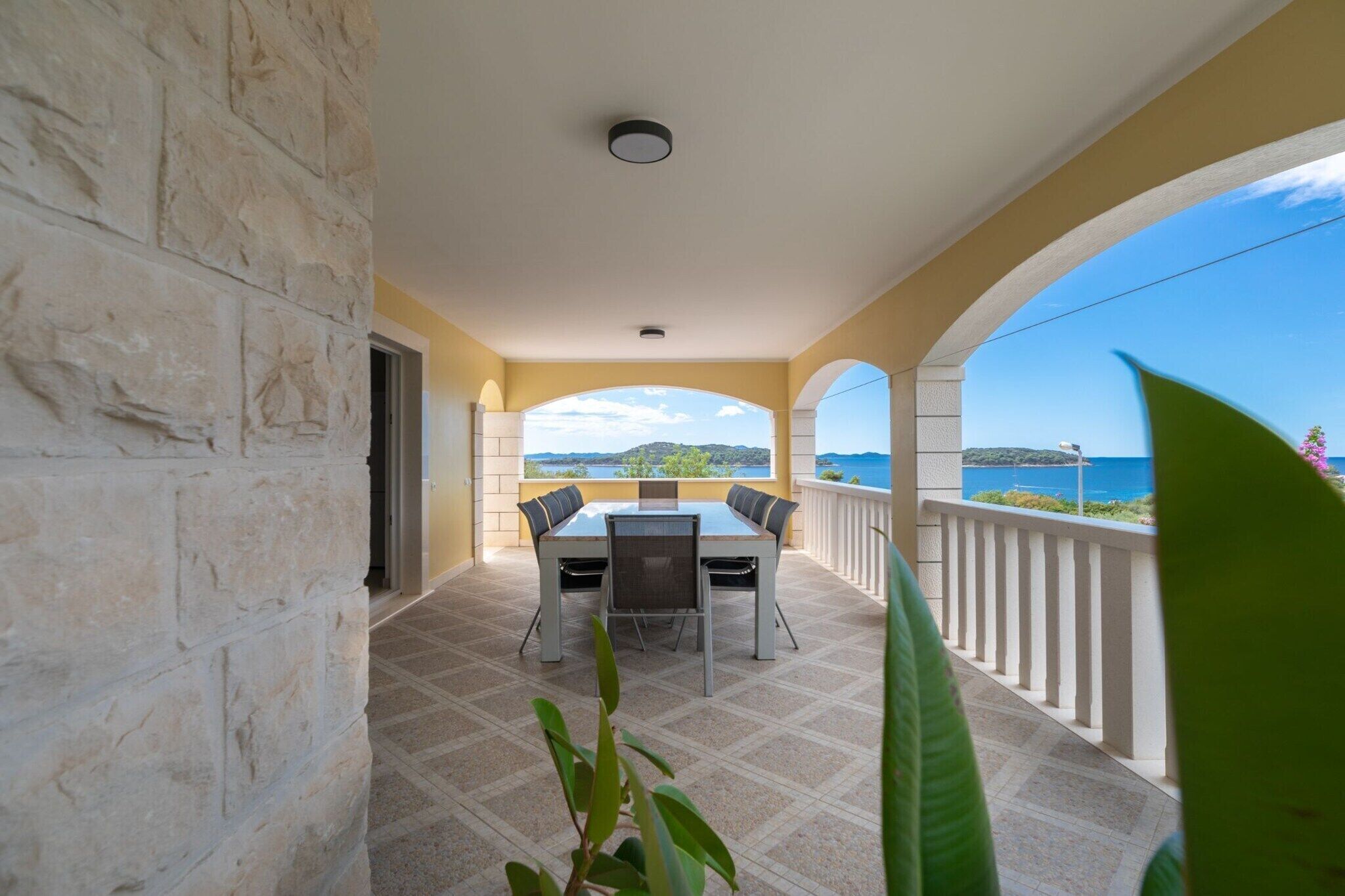 Ein Balkon mit Tisch und Stühlen, eine Steinmauer und Blick aufs Meer.