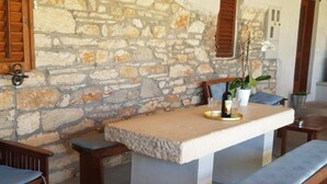A stone-walled room with a stone table, wooden benches, and a potted plant.