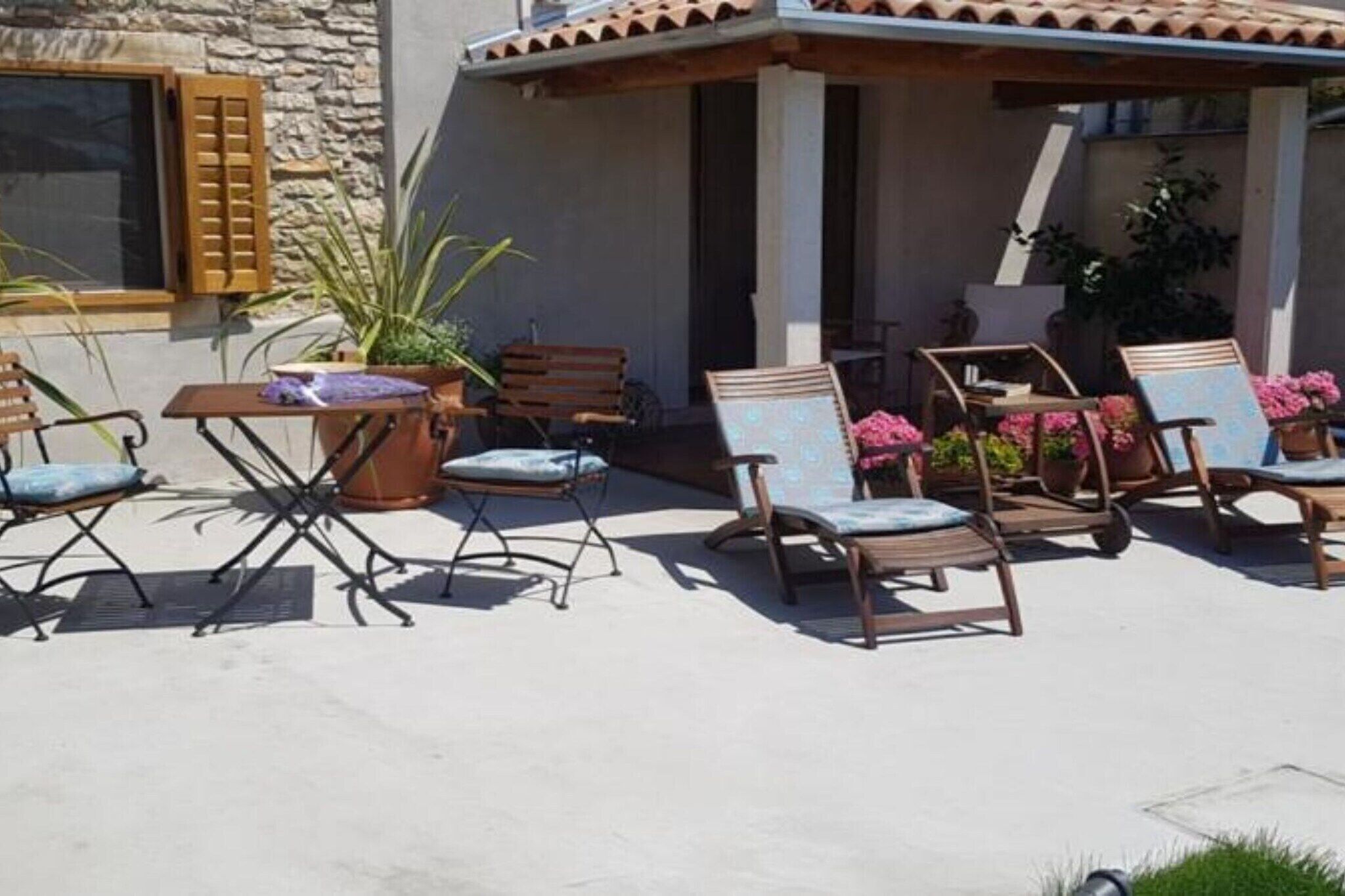 Un patio al aire libre con sillas y una mesa de madera, rodeado de macetas con plantas y flores.