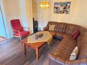 A living room with a brown leather sofa, a wooden coffee table, a red armchair, and a wall-mounted light fixture. - Spacious House, With Boat, in Beautiful Landscape (Aure)