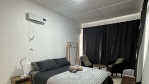 A modern bedroom with a bed, bedside table, lamp, air conditioning unit, and a chair. - Swansea Coastal Retreat near the sea and IGA (Swansea)