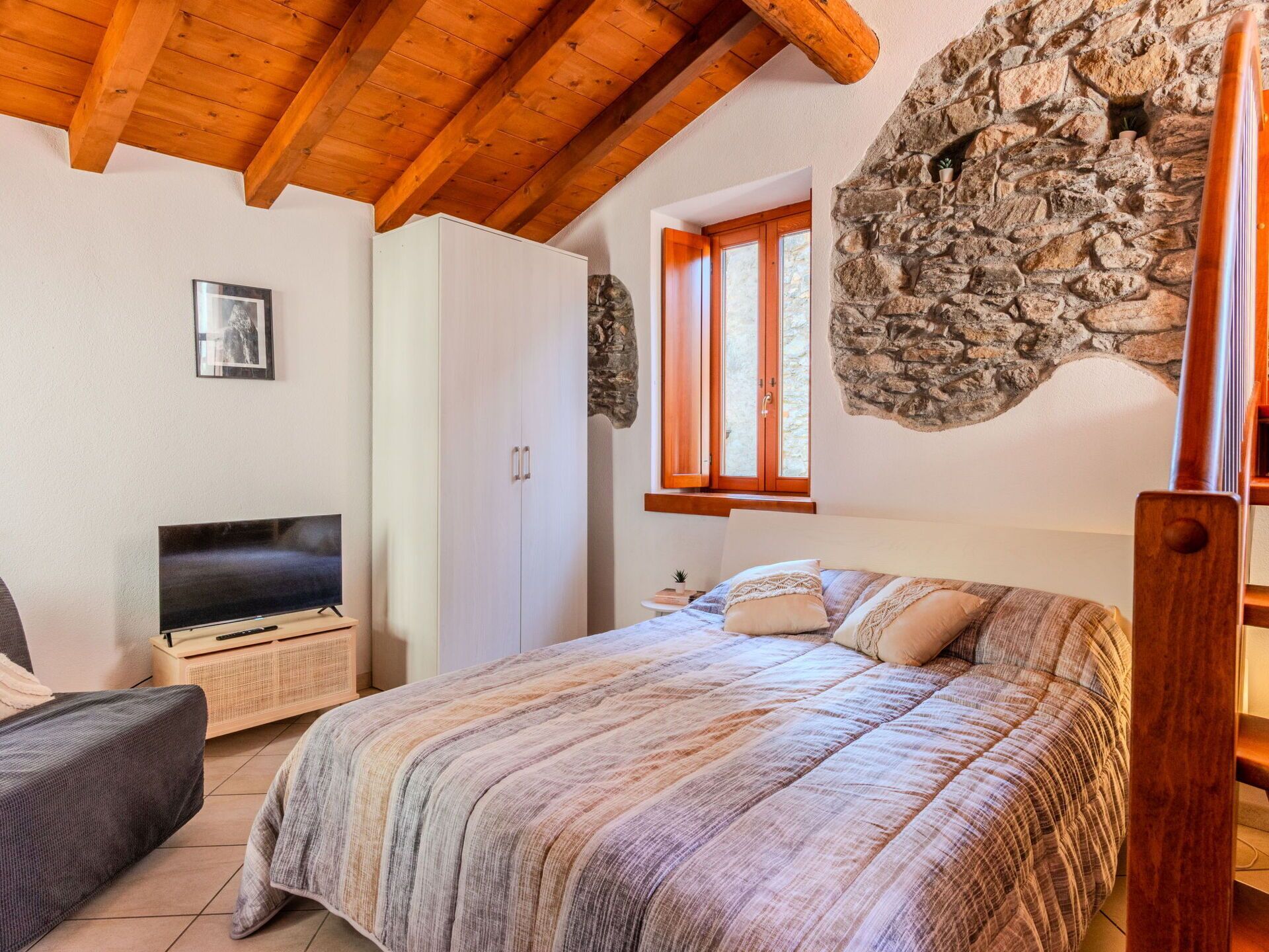Un dormitorio con cama, televisión, armario y pared de piedra.