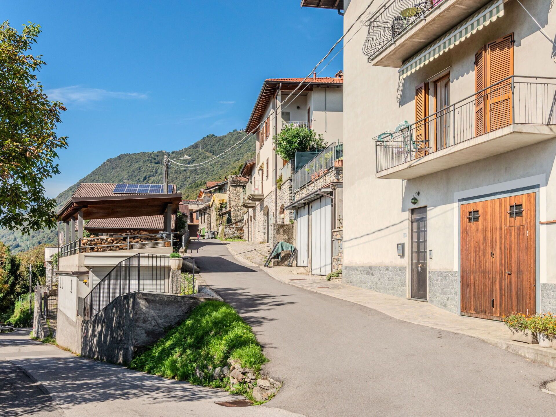 Une rue étroite bordée de bâtiments traditionnels en pierre, dont certains sont dotés de volets en bois et de balcons.