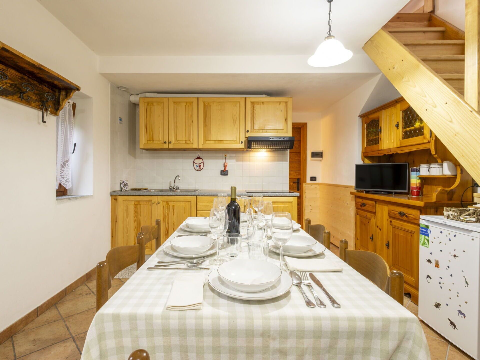 Un comedor con mantel a cuadros, armarios de madera y una cocina al fondo.