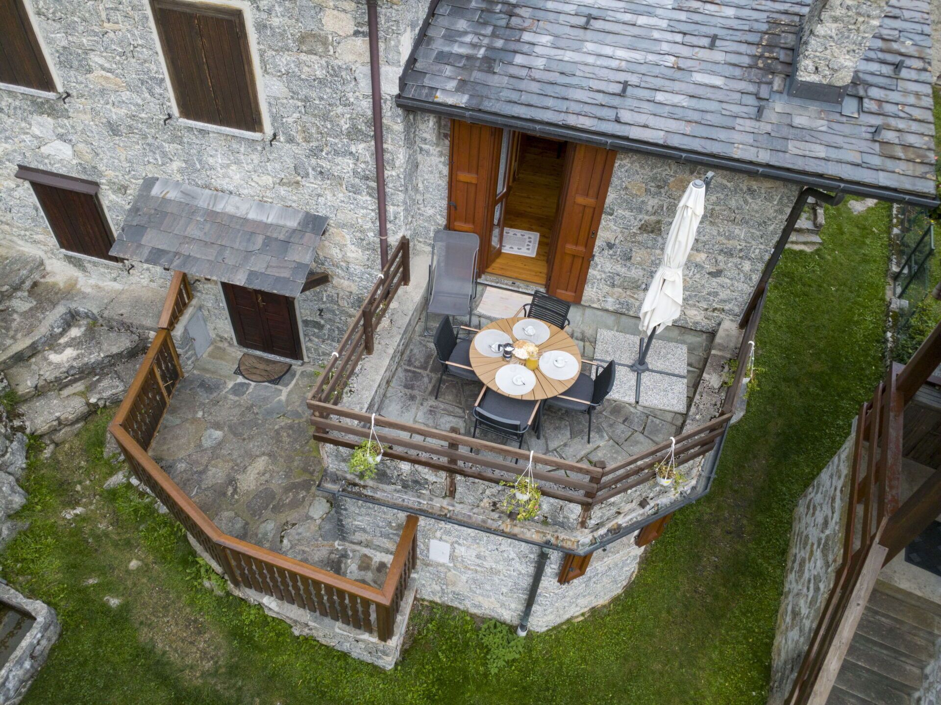 Ein Steinhaus mit einer kleinen Außenveranda, ausgestattet mit einem runden Tisch und Stühlen, einem Holzzaun und einer Rasenfläche.