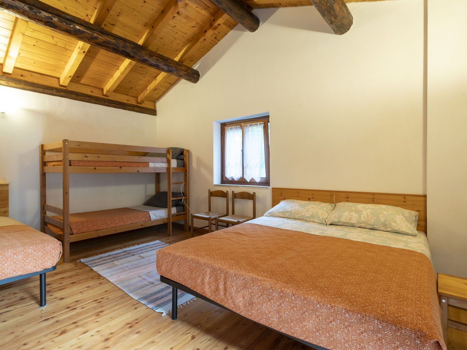 Een kamer met twee stapelbedden, een enkel bed, een raam met gordijnen en een houten plafond.