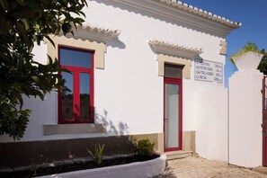 A building with a white facade, red doors, and a small garden area with a potted plant. - Studio dos Cantoneiros (Salir)