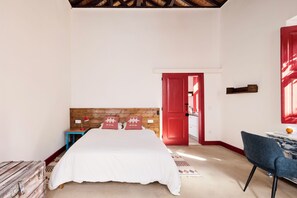 A bedroom with a wooden headboard, a bed with white bedding, a red door, a small table with a lamp, and a blue chair. - Studio dos Cantoneiros (Salir)
