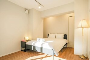 A bedroom with a bed, bedside table, lamp, and a door. - Mi-HOTEL ASAKUSA (Tokyo)