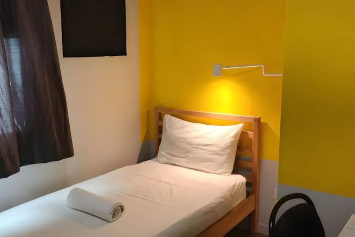 Un lit simple avec une tête de lit en bois, un oreiller blanc et une couverture soigneusement disposée.