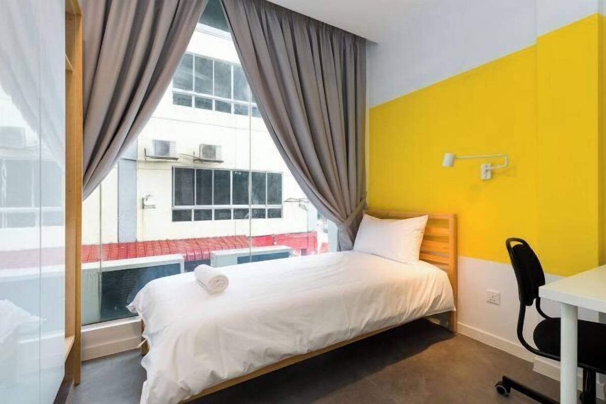 Ein Hotelzimmer mit Bett, Schreibtisch, Stuhl, einem Fenster mit Vorhängen und Blick nach draußen.