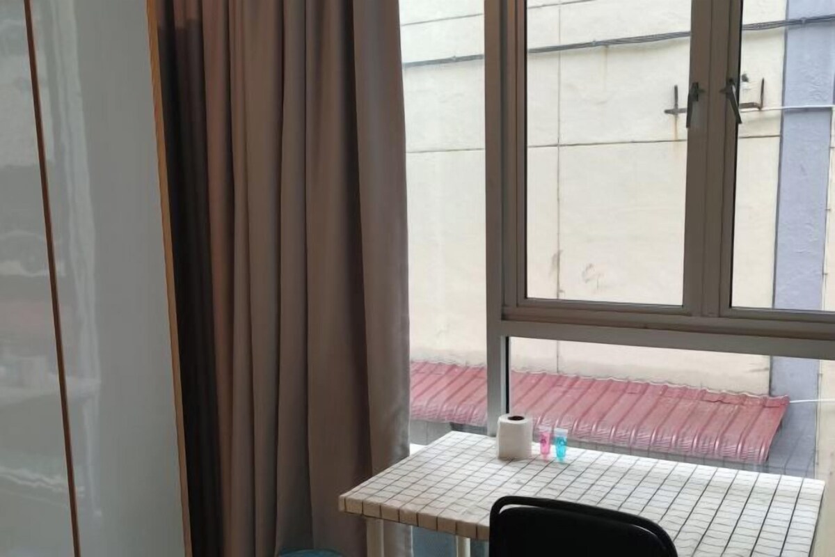 A room with a window, a table with a grid pattern, a chair, and a curtain.