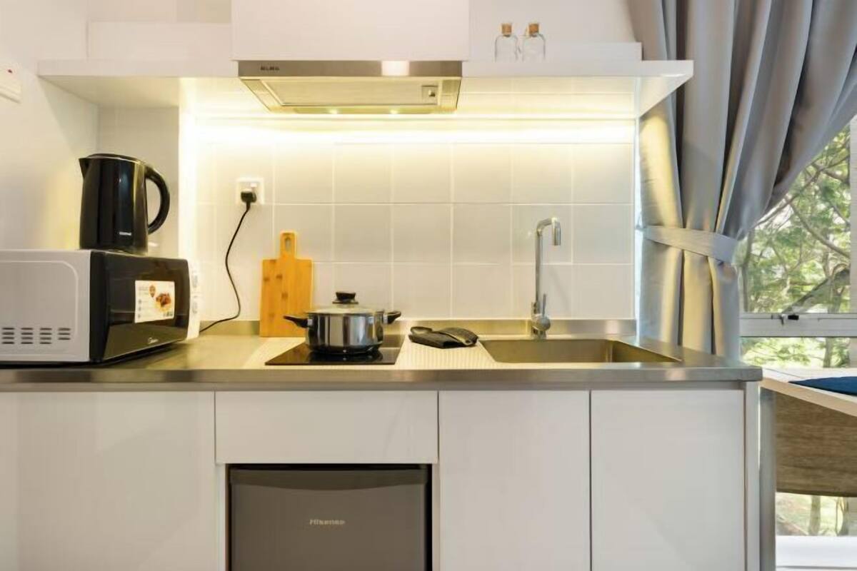 Eine moderne Küche mit Mikrowelle, Wasserkocher und Topf auf der Arbeitsplatte, einem eingebauten Geschirrspüler und einem Fenster mit Vorhängen.