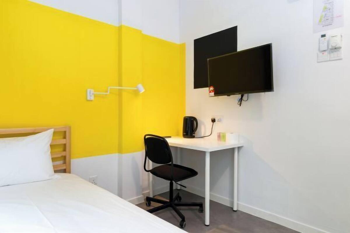 Ein Hotelzimmer mit einem Bett, einem Schreibtisch, einem Sessel, einem Fernseher und einem Wandregal.
