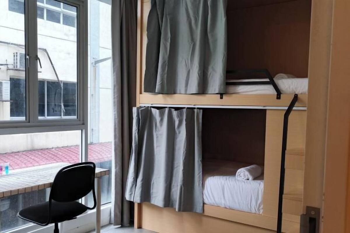 Ein Schlafsaalzimmer mit Etagenbetten, einem Fenster mit Vorhängen und einem Stuhl am Fenster.