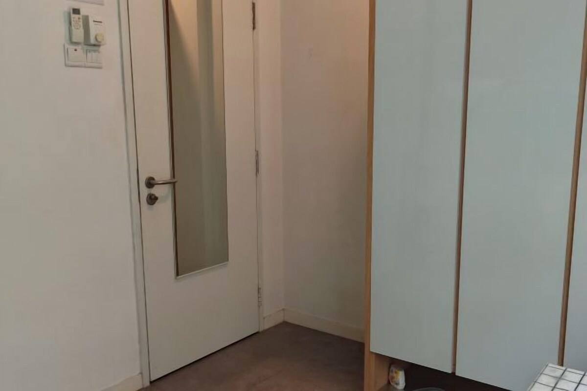A narrow hallway with a white door featuring a frosted glass panel and a small electrical outlet on the wall.