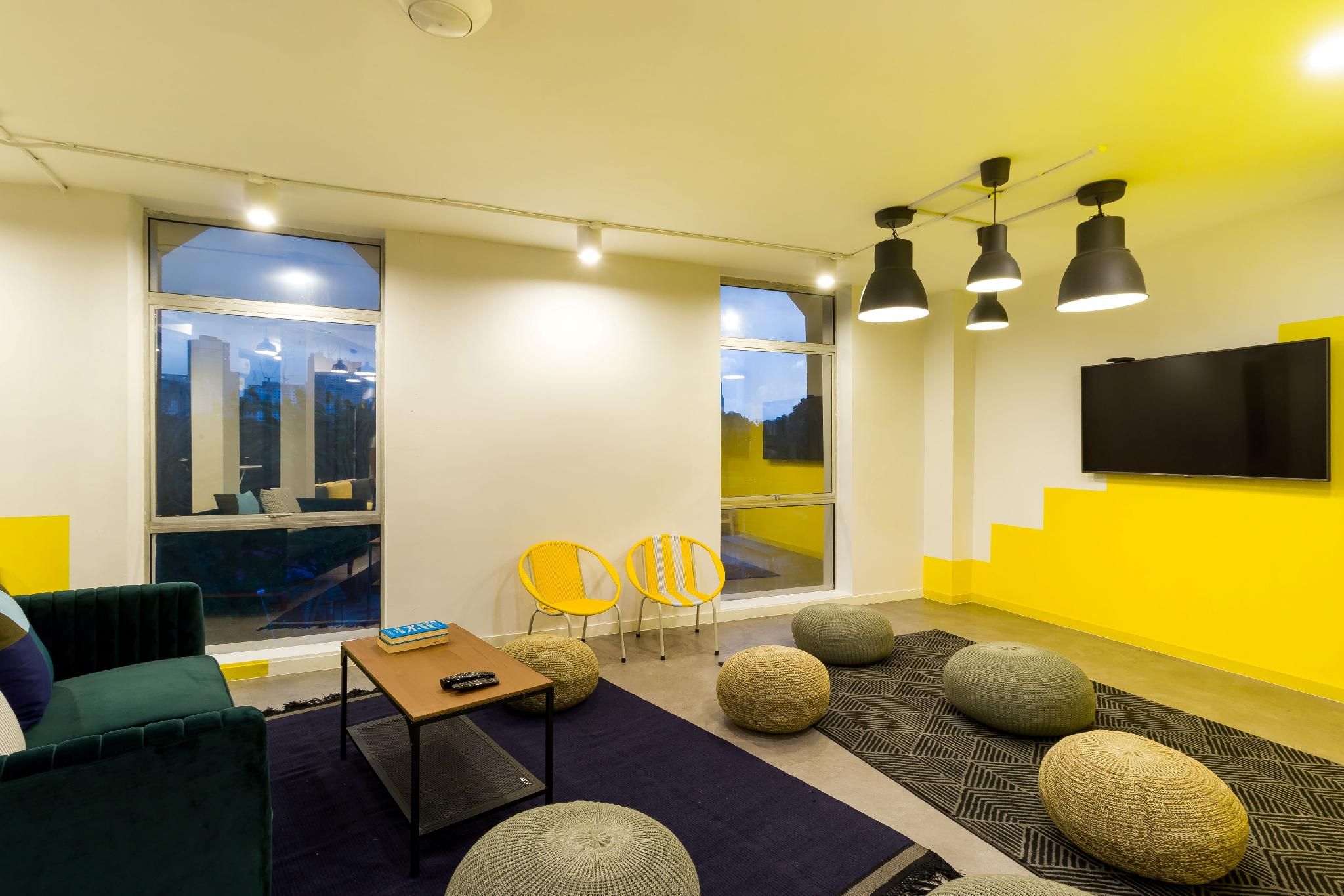 A modern living room with a flat-screen TV, two yellow chairs, a green sofa, and a coffee table.