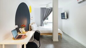 A hotel room with a bed, a desk with a laptop, a chair, a TV, and a window with curtains. - Upstairs Downstairs Co Living Kampung Pandan (Kuala Lumpur)