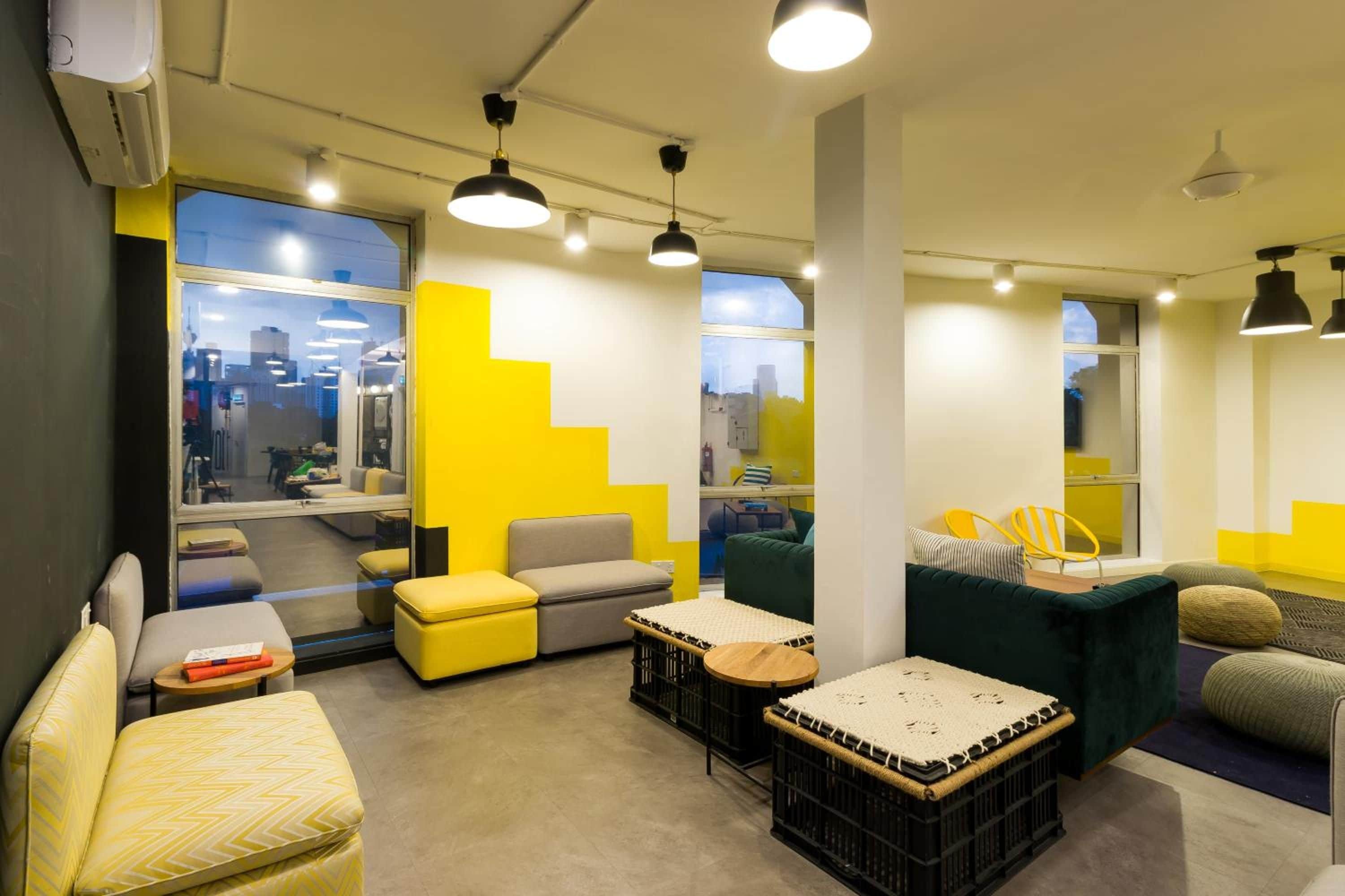Ein modernes Interieur mit verschiedenen Sitzmöglichkeiten, darunter eine Couch, Stühle und eine Bank. Große Fenster bieten Blick auf die Stadtlandschaft.