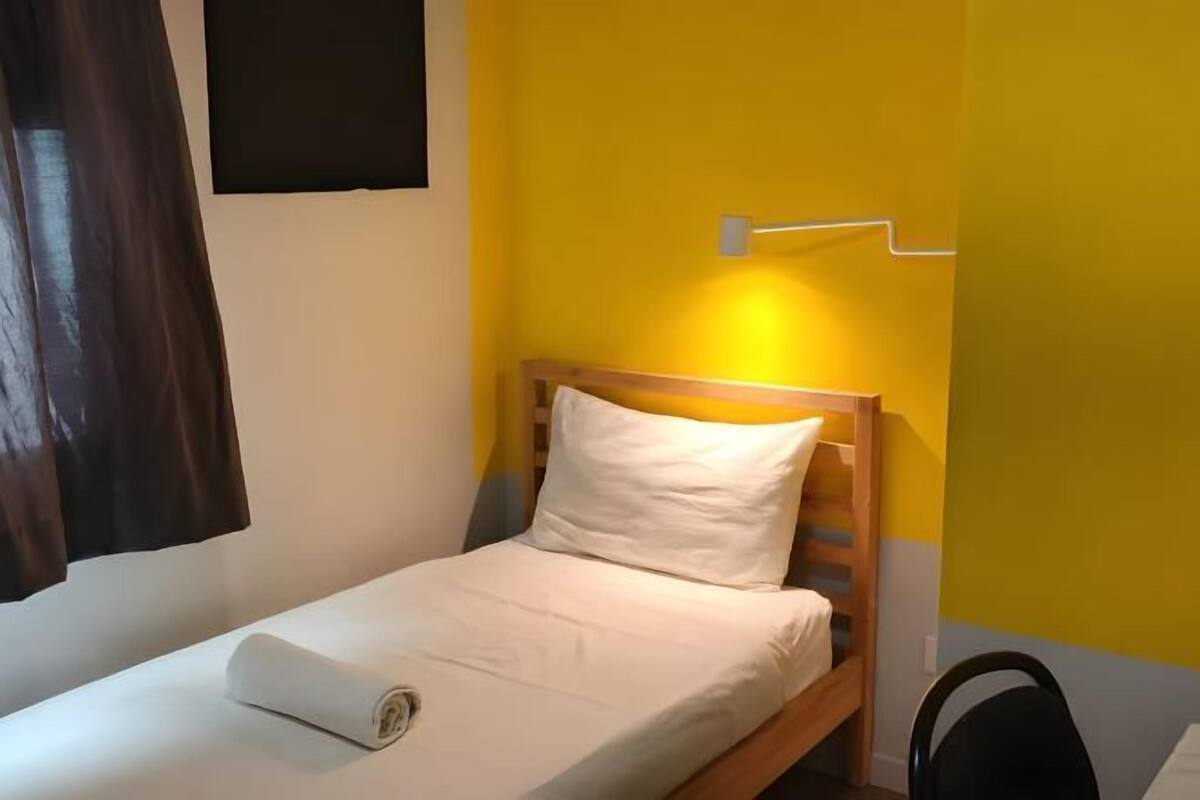 Ein Einzelbett mit Holz-Kopfstück, einem weißen Kissen und einer ordentlich bezogenen Bettdecke.