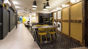 A modern hotel lobby with a long corridor, a dining area with yellow chairs, and a visible washing machine. - Upstairs Downstairs Co Living Kampung Pandan (Kuala Lumpur)