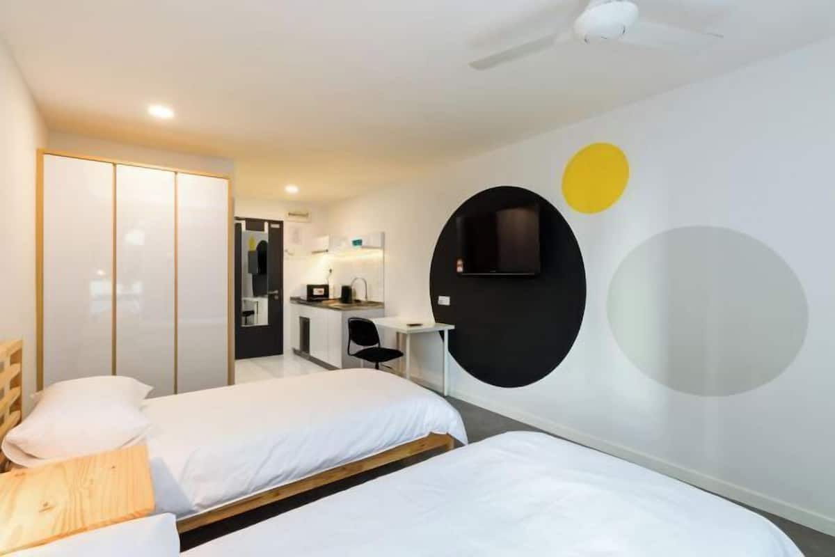 A modern hotel room with two beds, a desk, a chair, and a TV mounted on the wall.