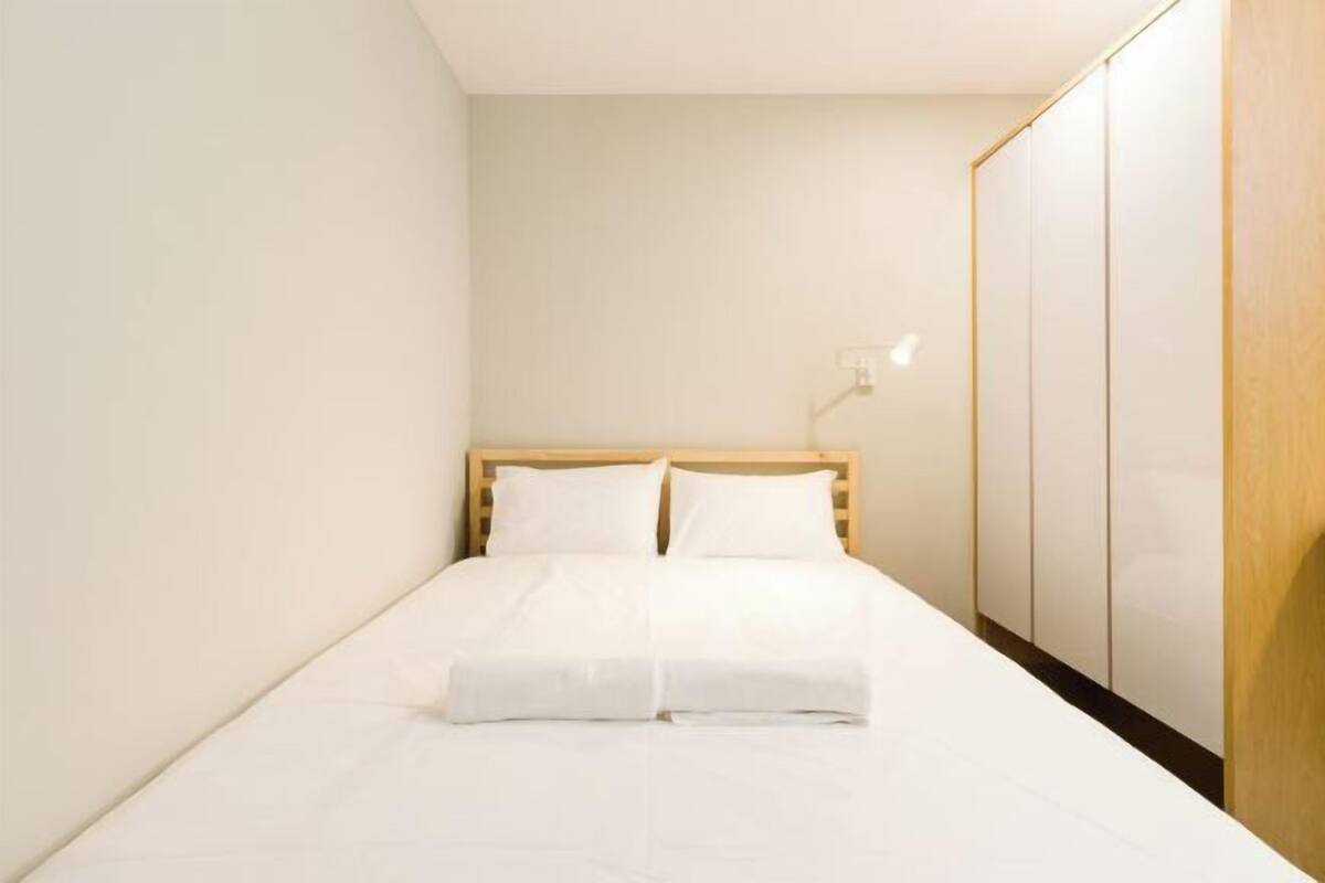 Ein ordentlich gemachtes Bett in einem kleinen Zimmer mit einem Holzkopfteil, einem Kleiderschrank und einer Wandleuchte.
