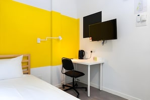 Une chambre d’hôtel équipée d’un lit, d’un bureau, d’une chaise, d’un téléviseur à écran plat et d’un radiateur fixé au mur.