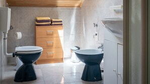 Un baño moderno con dos inodoros negros, un armario de madera y un lavamanos blanco.