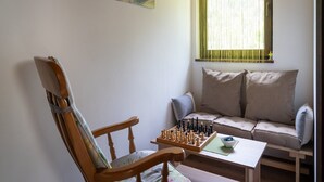 Una habitación acogedora con una silla de madera, un sofá y un tablero de ajedrez sobre una mesita.