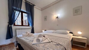 A neatly made bed with rolled towels, a bedside table with a lamp, and a window with blue curtains. - Apartments Butković - One Bedroom Apartment (A2) (Novi Vinodolski)