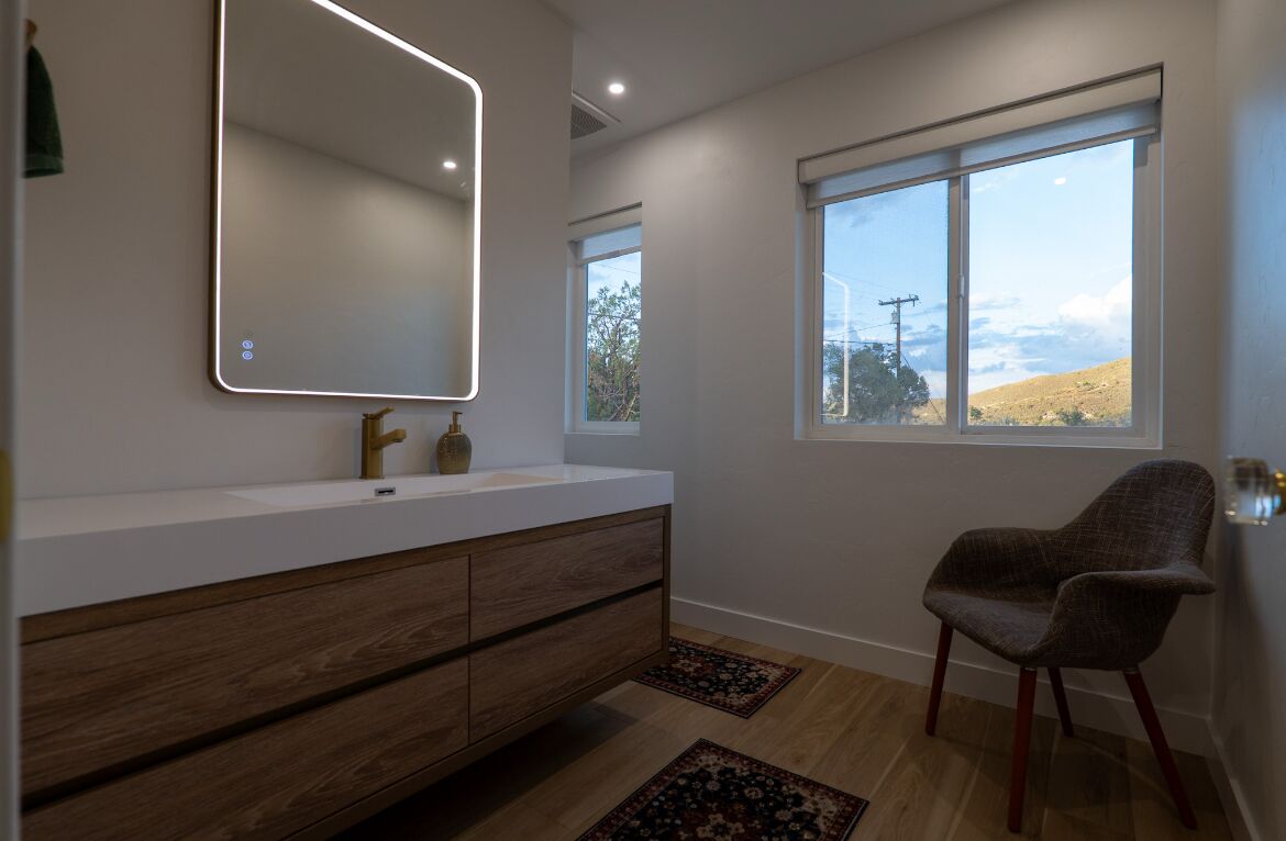 Een moderne badkamer met een grote spiegel, een houten wastafelmeubel en een stoel.