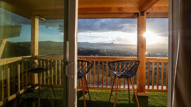 Un balcón con dos sillas y baranda de madera, con vistas a un paisaje pintoresco con montañas y un atardecer.