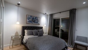 Un dormitorio moderno con una cama grande, un ventanal de vidrio que da a un balcón y una mesita auxiliar.