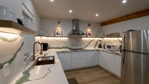 Una cocina moderna con armarios blancos, un refrigerador de acero inoxidable, un microondas integrado y una encimera de mármol.