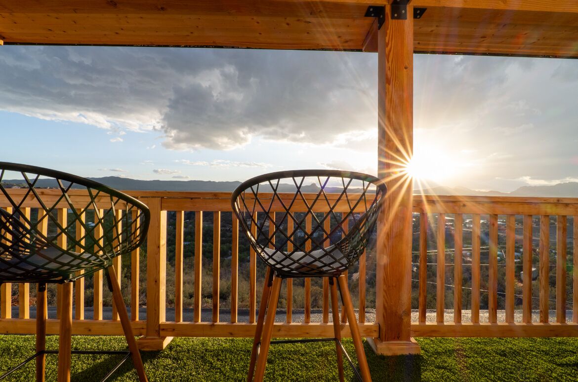 Twee stoelen gericht op een houten terras met uitzicht op bergen en een ondergaande zon.