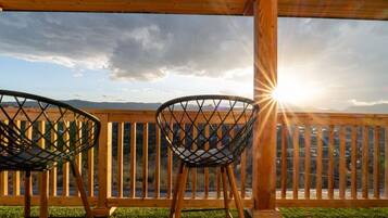 Twee stoelen gericht op een houten terras met uitzicht op bergen en een ondergaande zon.