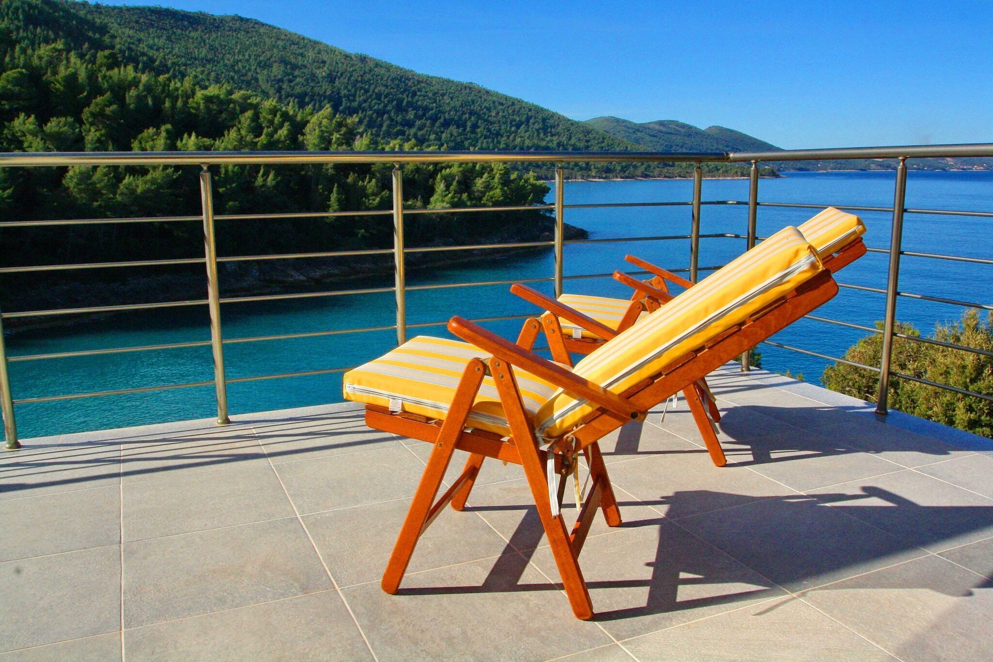 Une terrasse avec deux chaises longues donnant sur une étendue d’eau et une colline boisée.