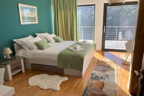 A bedroom with a bed, a nightstand, a white furry rug, and a view of a balcony.