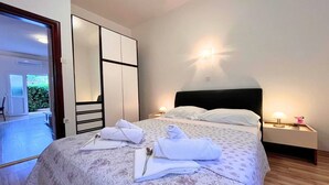 A neatly made bed with towels and a rose, a bedside table with a lamp, and a view of a balcony.