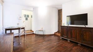A living room with a wooden dining table, clear plastic chairs, a small white table, and a TV on a wooden cabinet. - Easylife - Milano - Carpoforo 5 - Brera (Milano)