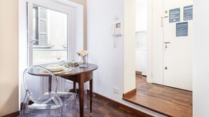 A room with a wooden floor, a dining table with clear chairs, a small vase with a flower, and a white door with a window and a wall-mounted phone. - Easylife - Milano - Carpoforo 5 - Brera (Milano)