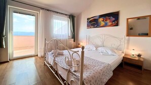 Un dormitorio con cama, mesita de noche, un cuadro y vista al mar a través de una ventana.