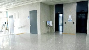 Eine helle, moderne Lobby mit glänzendem Boden, einer kleinen Staffelei mit einem Plakat und zwei Aufzügen.