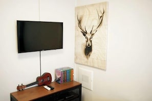 A wall-mounted TV, a ukulele, and a collection of books on a wooden shelf. - Well Stay Hotel (Incheon)