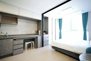Ein modernes Hotelzimmer mit Küchenzeile, einem Bett und einem großen Fenster mit Vorhängen.