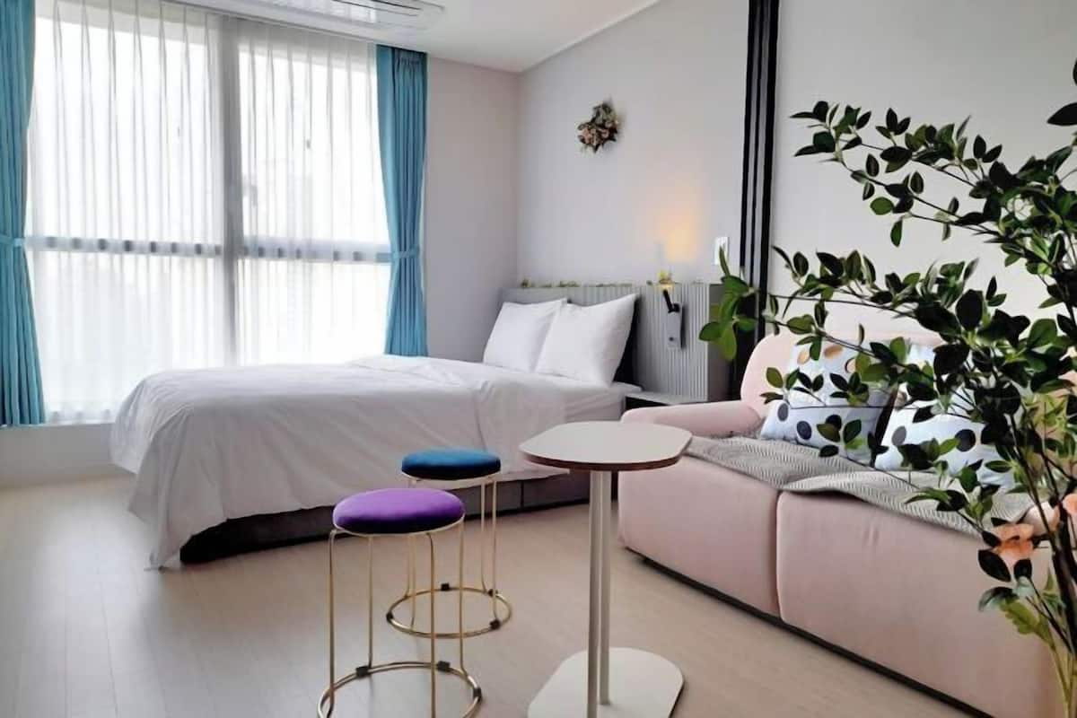 Et moderne hotelværelse med seng, to skamler, et lille bord, en sofa og et stort vindue med gardiner.