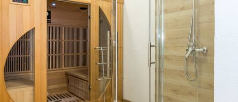 A sauna room with a wooden door, a glass shower enclosure, and a control panel.