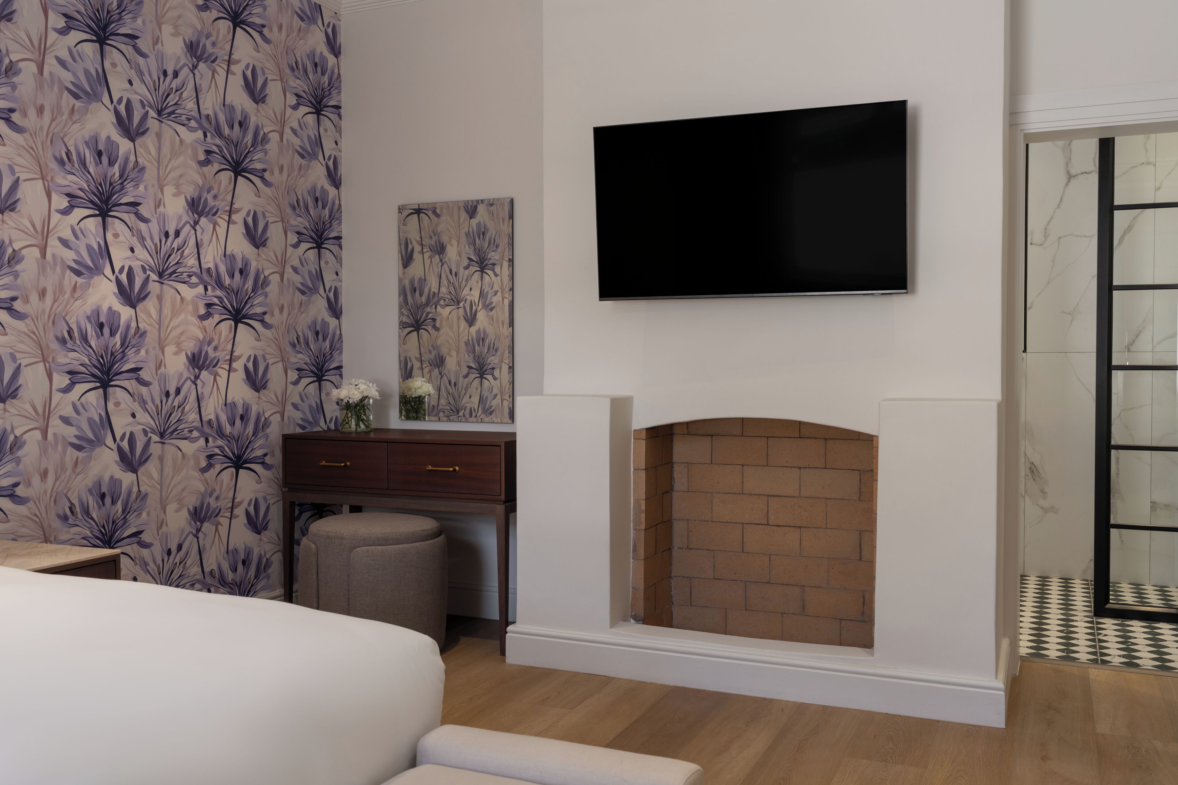 A bedroom with a bed, a dresser, a TV mounted on the wall, and a fireplace.